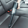 Ruční tyčový vysavač umístěný na sedadle automobilu s černým čalouněním, určený pro čištění interiéru vozu.