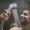 Muž se spokojeným úsměvem drží sprchovou hlavici s filtrem, ze které proudí voda v hustých proužcích.