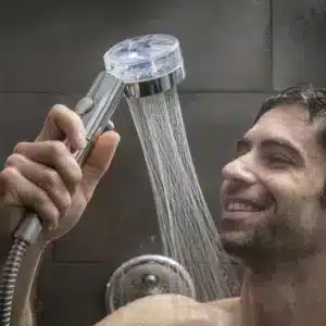 Muž se spokojeným úsměvem drží sprchovou hlavici s filtrem, ze které proudí voda v hustých proužcích.
