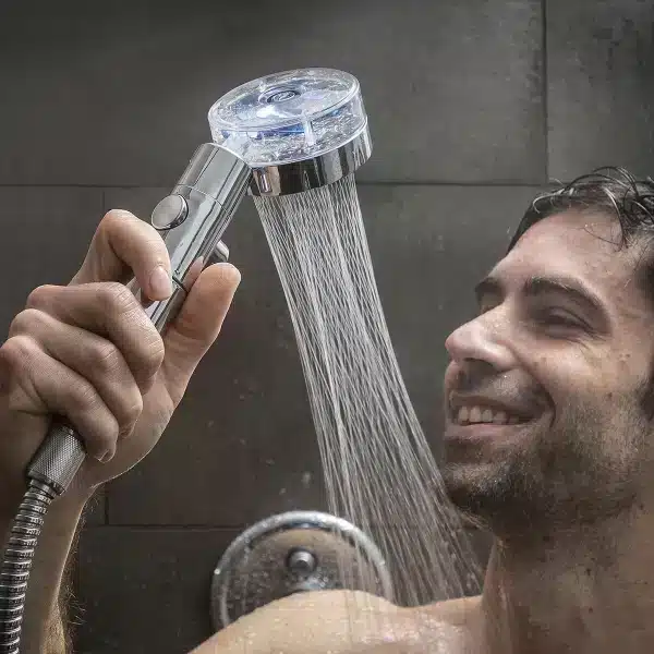Muž se spokojeným úsměvem drží sprchovou hlavici s filtrem, ze které proudí voda v hustých proužcích.