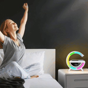 Žena sedící na posteli s nataženou rukou a úsměvem vedle barevného digitálního budíku ve tvaru písmene G s RGB podsvícením.