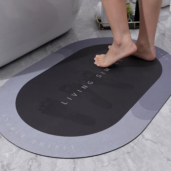 Černá absorpční koupelnová podložka s nápisem "Living Sm" pod bosou nohou na světlé podlaze, designovaná pro rychlé sušení a protiskluzové vlastnosti.