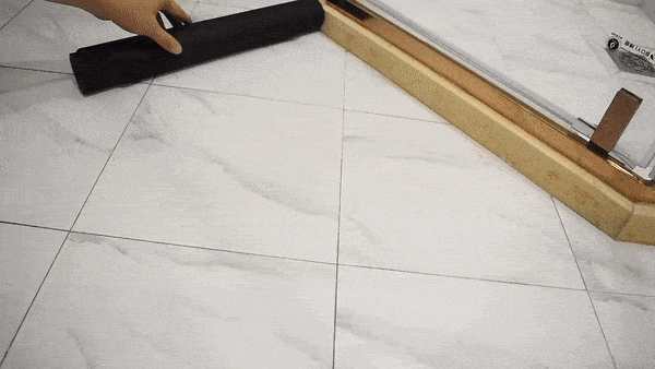 While I understand your request, the image actually shows some construction or tiling work. The image depicts a marble or stone tile floor with gridlines, and part of a hand holding a black roller or tool, alongside what appears to be a wooden straightedge or ruler. This looks like a flooring installation or measurement process, not a bath mat as described in the product description.
Would you like me to describe what I actually see in the image?