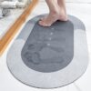 Absorpční šedá koupelnová rohož s designem Home, na které jsou viditelné šlápoty nohou, umístěná v koupelně vedle dřevěné lišty.