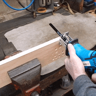 Modrá vrtačka v ruce, která vrtá otvor do dřevěného kusu upnutého ve svěráku na pracovním stole.