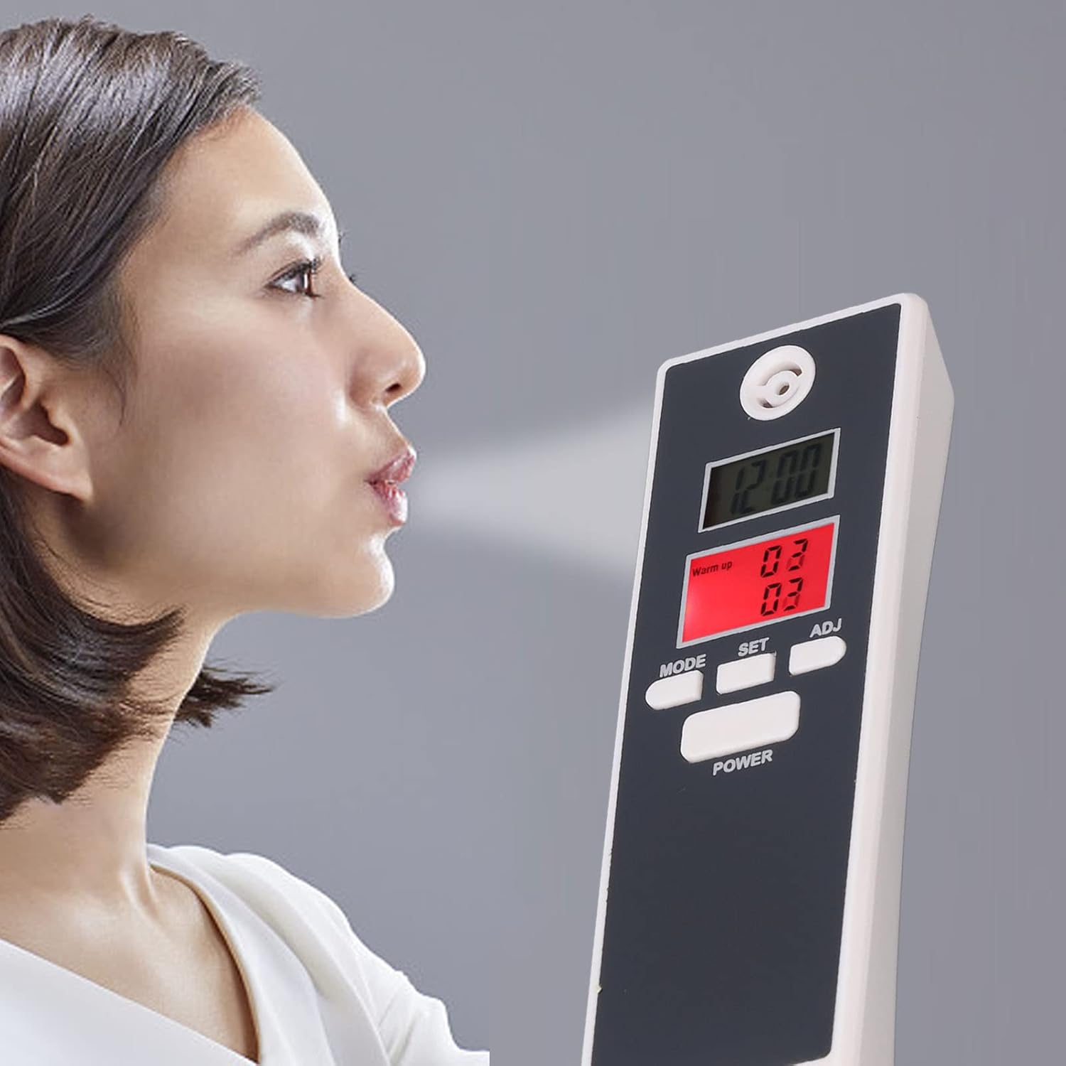 A person in profile blowing towards a digital breath alcohol tester device, which displays readings on its LCD screen against a neutral gray background.
