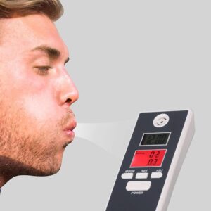 A person blowing into a digital breathalyzer device to test their blood alcohol content, with the device displaying readings on its screen.