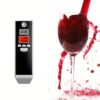 Digitální alkohol tester s černým designem vedle sklenice červeného vína s rozstříknutou tekutinou, zobrazující elektronické měření hladiny alkoholu.