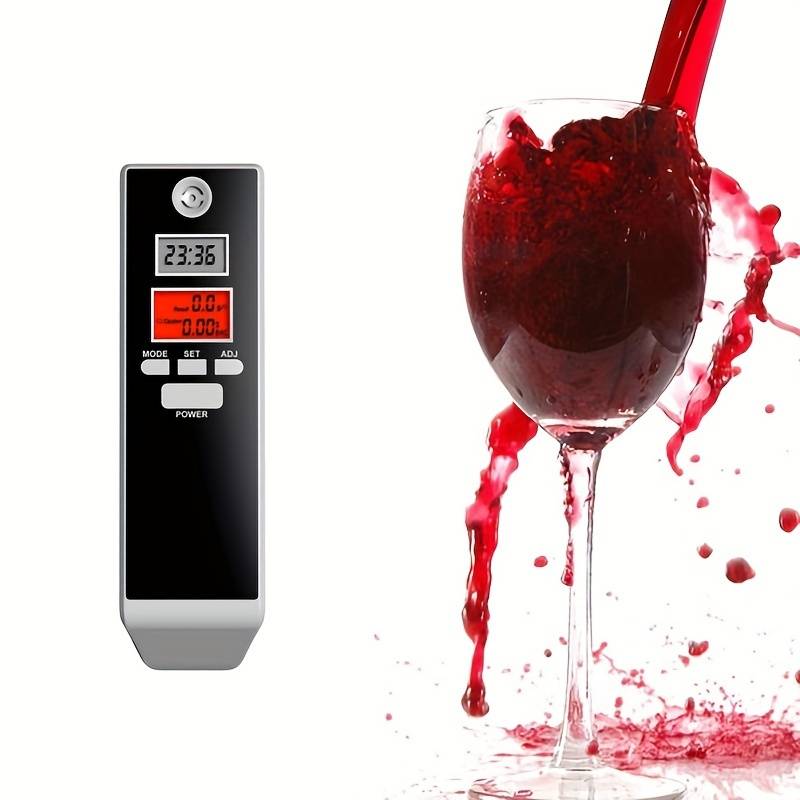 Digitální alkohol tester s černým designem vedle sklenice červeného vína s rozstříknutou tekutinou, zobrazující elektronické měření hladiny alkoholu.