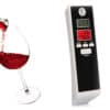 Digitálny alkohol tester s displejom vedľa pohára červeného vína, slúžiaci na rýchle a jednoduché zmeranie hladiny alkoholu v dychu pred šoférovaním.