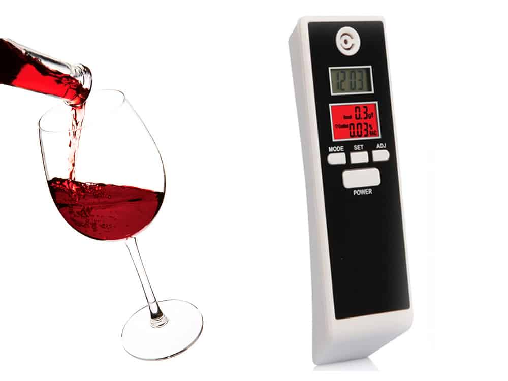 Digitálny alkohol tester s displejom vedľa pohára červeného vína, slúžiaci na rýchle a jednoduché zmeranie hladiny alkoholu v dychu pred šoférovaním.