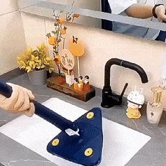 The image shows a modern kitchen sink area with a unique triangular blue mop and some decorative items like a yellow vase with flowers in the background.