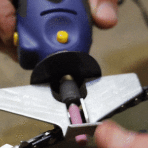Detailní záběr na elektrickou brusku nebo gravírovací nástroj s nasazeným brusným nástavcem, který je používán k opracování kovového nebo jiného povrchu.