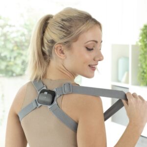Žena s bluetooth headsetem a šedým popruhem na rameni, v neutrálním prostředí s výhledem do zeleně.