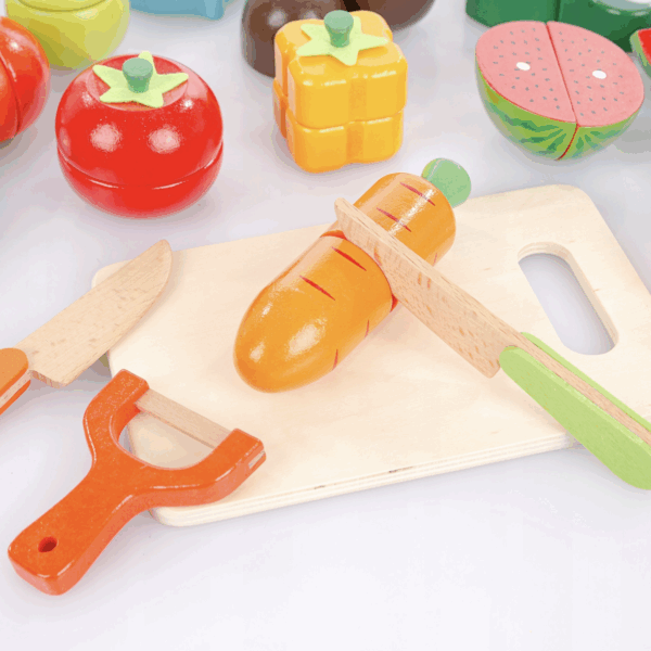 Dřevěné hračky ovoce a zeleniny s krájecí prkénkou a nástroji, včetně rajčete, papriky, melounu a mrkve, simulující krájení potravin pro děti.