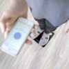Pohled shora na osobu v ponožkách s motivem a mobilní telefon s rozmazaným modrým displejem, položené na světlé podlaze.