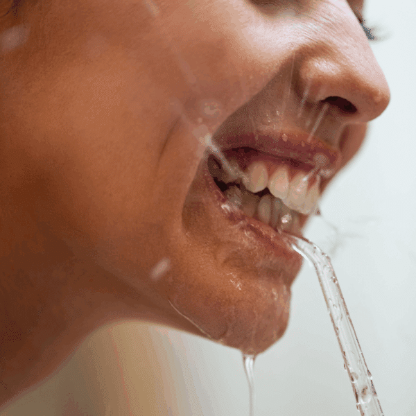 Detailní pohled na dolní část obličeje, kde z úst stéká tenký proud vody, zobrazující kapky a lesk na rtech a kůži.