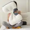 Ergonomický bílo-šedý masážní polštář ve tvaru asymetrického tvaru, který někdo drží v náručí a sedí na posteli v pohodlné póze.