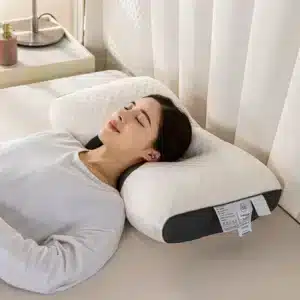 Bílý ergonomický masážní polštář s černým lemováním, na kterém odpočívá žena s černými vlasy v bílém oblečení, s očima zavřenýma a klidným výrazem.