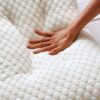 A hand pressing into a white, textured ergonomic massage cushion with a honeycomb-like pattern, demonstrating its soft and supportive surface.