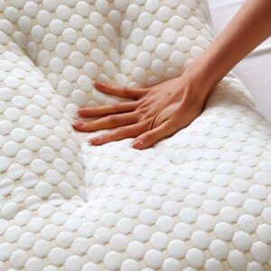 A hand pressing into a white, textured ergonomic massage cushion with a honeycomb-like pattern, demonstrating its soft and supportive surface.
