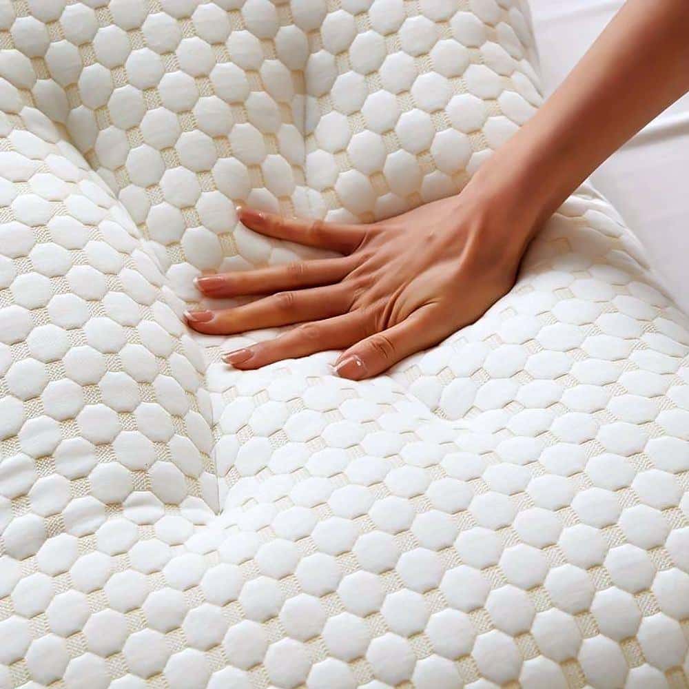 A hand pressing into a white, textured ergonomic massage cushion with a honeycomb-like pattern, demonstrating its soft and supportive surface.