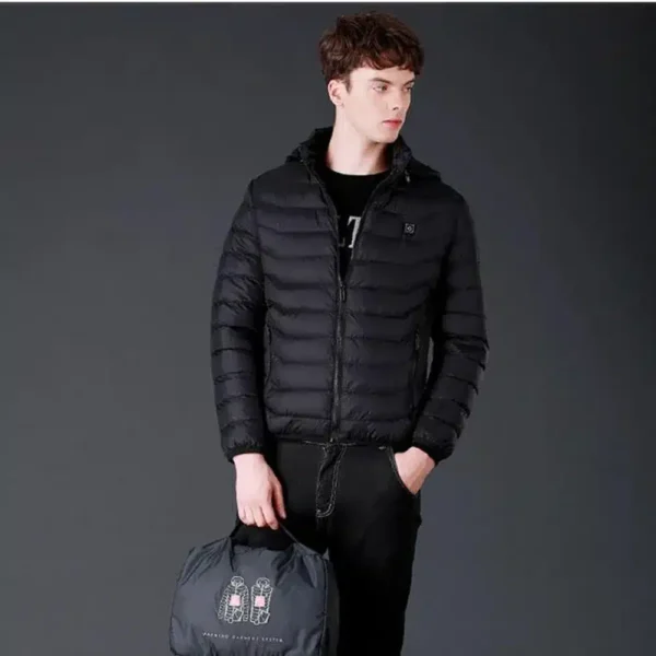 Mladý muž oblečený v černé prošívané bundě s kapucí, černých kalhotách a s černou taškou v ruce, pózující na tmavém pozadí ve studiu.