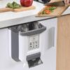 Kuchyňská skříňka s vestavěným košem na odpadky, kde někdo krájí zeleninu na dřevěném prkénku a připravuje ingredience do připravovaného jídla.