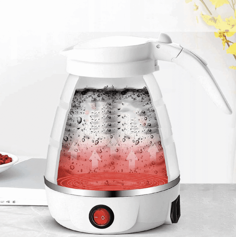 Elektrická skleněná konvice s červeným osvětlením dna, naplněná vodou se vzduchových bublinkami, umístěná na bílém podstavci s vypínačem.