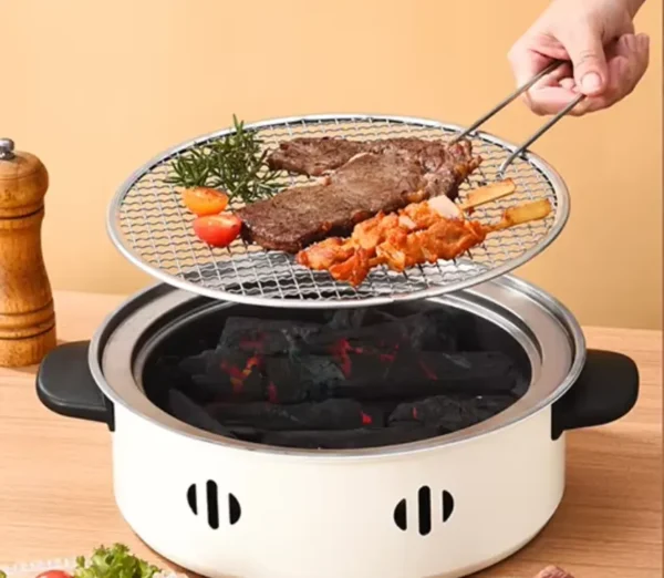 Japonská přenosná gril s mřížkou, na které se opékají kusy masa a zeleniny nad žhnoucím dřevěným uhlím v bílém ocelovém těle grilu.