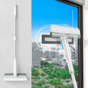 Bílý čistič oken s ostřikovačem zachycený při čištění skleněné tabule, s venkovní zahradou v pozadí a dynamickým proudem vody kolem čisticí hlavy.