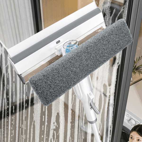 Bílý čistič oken s šedou textilní stranou, zavěšený na zasklené ploše s kapkami vody, určený pro snadné a účinné mytí skleněných povrchů.