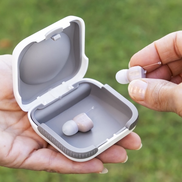 Bílé bezdrátové sluchátko s nabíjecím pouzdrem, z kterého je vyjímán jeden z miniaturních sluchátek.