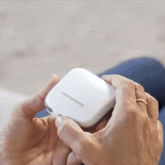 Ruka drží bílé bezdrátové sluchátko Samsung, zachycená v detailu na modrém pozadí.