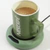 Zelený Nescafé hrnček naplnený čerstvou kávou, položený na zelenej podložke na ohrev a udržanie teploty nápoja.