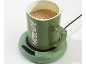 Zelený Nescafé hrnček naplnený čerstvou kávou, položený na zelenej podložke na ohrev a udržanie teploty nápoja.