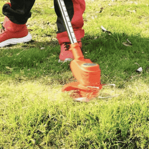 Sekání trávy pomocí elektrické strunové sekačky v oranžové barvě, zachycené v pohybu na zelené trávě s několika padlými listy.