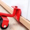 Červený malířský váleček s černým kolečkem, který je umístěn u dřevěné lišty na světlé podlaze, připravený na malování stěn.