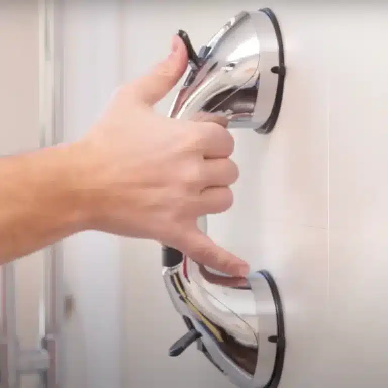 Chromová ruční žehlička s lesklým povrchem, zachycená při žehlení bílého kusu oblečení v pozadí.