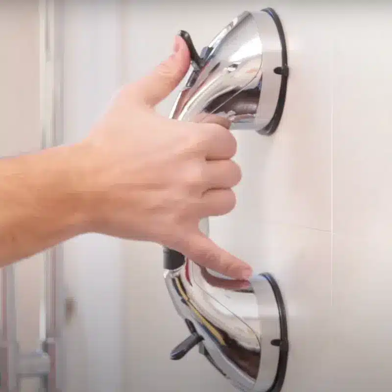 Chromová ruční žehlička s lesklým povrchem, zachycená při žehlení bílého kusu oblečení v pozadí.