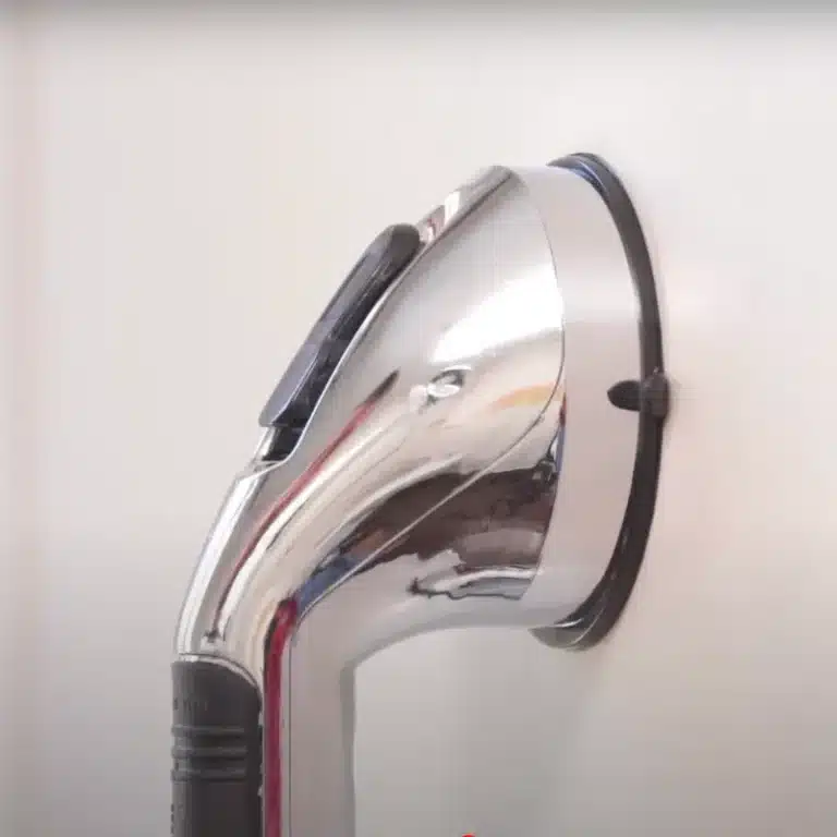 Chromovaná žehlička s lesklým kovovým povrchem a černou rukojetí, fotografovaná z úhlu proti světlému pozadí.