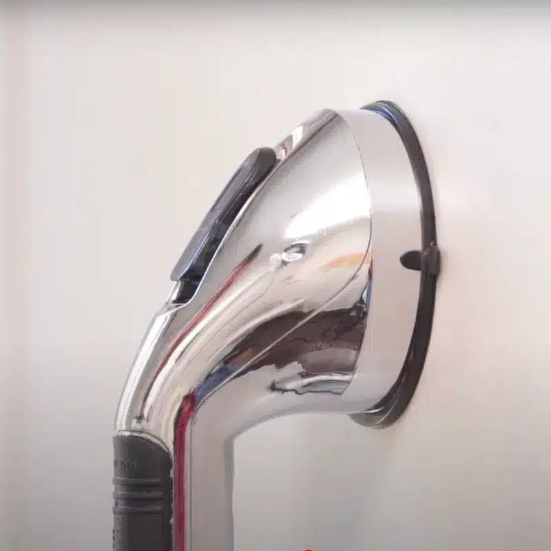 Chromovaná žehlička s lesklým kovovým povrchem a černou rukojetí, fotografovaná z úhlu proti světlému pozadí.