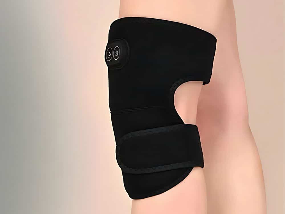 Černá ortéza na koleno s technologickým designem, připevněná na světlém pozadí zobrazující část lidské nohy.