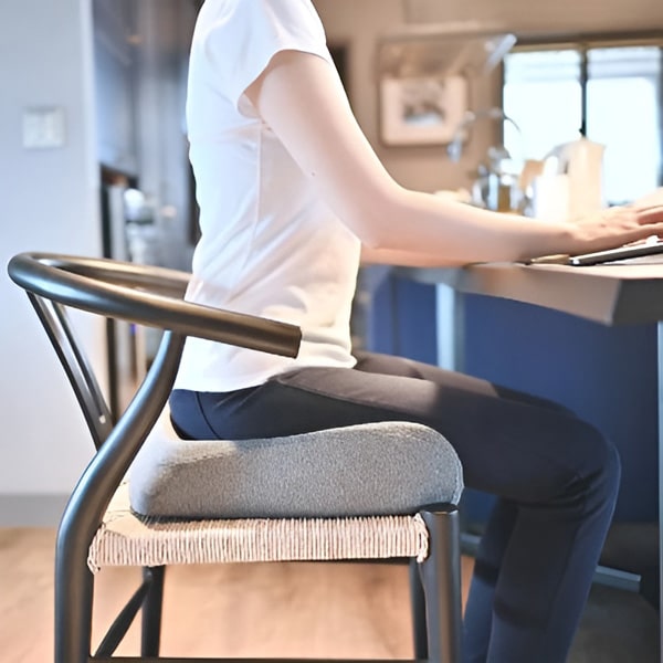 Osoba sedící na černé designové židli v kuchyni, oblečená v bílém tričku a tmavých kalhotách, pracující na klávesnici.
