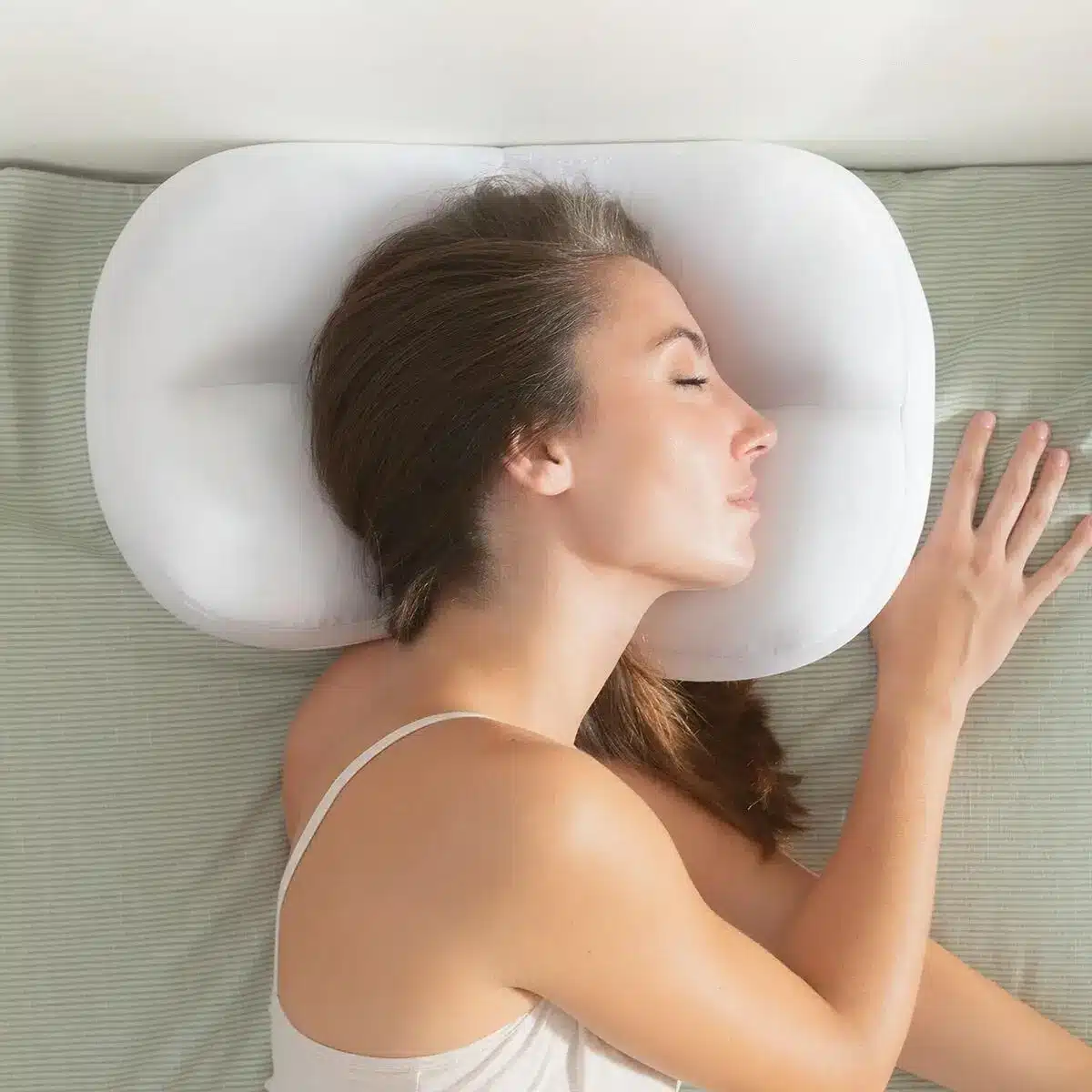 Bílý ergonomický polštář ve tvaru mraku, na kterém spí žena s zavřenýma očima, podporující správné držení hlavy a krku během spánku.