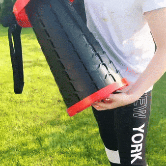 Černé fitness břemeno s červenými okraji v ruce osoby s černými legínami s nápisem New York, stojící na zelené trávě.