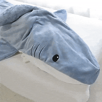 Modrý plyšový žralok s černýma očima, který leží na bílém povrchu a vypadá roztomile a měkce.