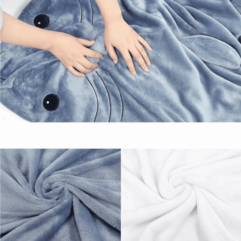 Modrá měkoučká deka ve tvaru žraloka s černýma očima, zachycená rukama v detailu textury froté látky v modré a bílé barvě.
