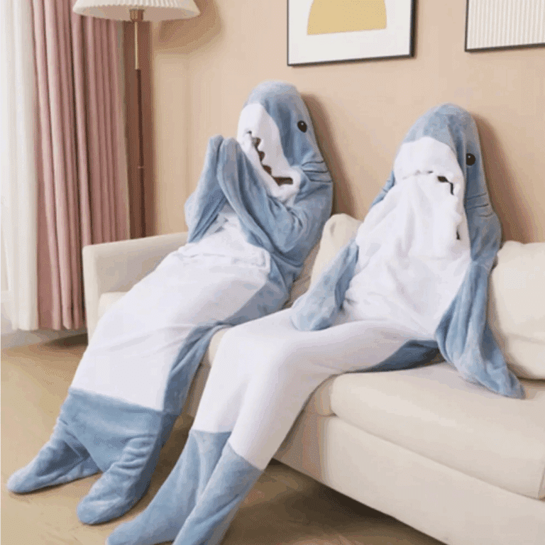 Dva plyšové žraloci v modrobílém provedení sedící vedle sebe na světlé pohovce v útulném pokoji s pastelovou výmalbou.