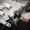 Adaptér na elektrickou vrtačku umožňující řezání trubek nebo jiných materiálů, zobrazující ruku držící vrtačku s připojeným řezacím nástavcem vedle několika bílých trubek.